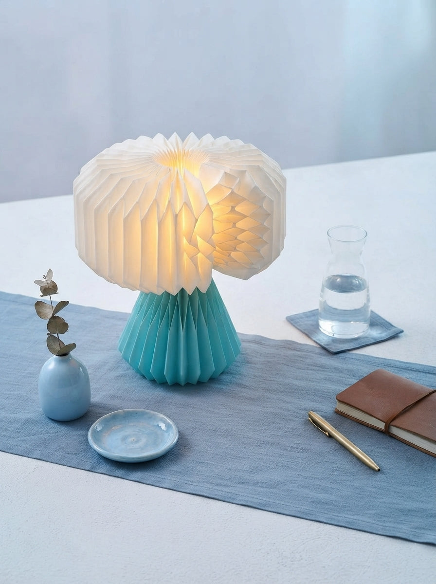 A magnetic foldable paper lamp partially opened on a surface with dusty blue and sky blue decorative accents.